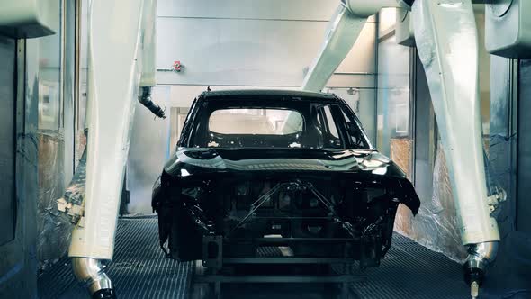 Automotive Painter Robots Spray Painting a Car Black at a Car Factory