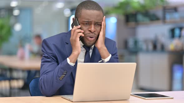 African Businessman with Laptop Angry on Smartphone in Office 