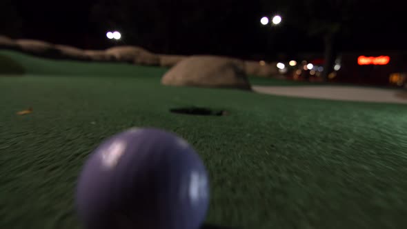 A purple mini golf ball falls into the golf hole and bounces in the pocket on a course.