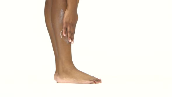 Woman Applying Moisturizer Cream on Leg. White. Close Up