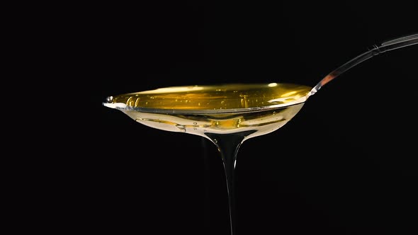 Pouring fresh honey from metal spoon over black background