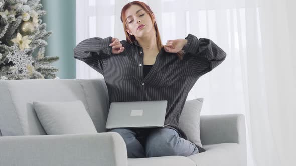 Overworked Woman Closing Laptop and Stretching Sitting on Couch on New Year's Eve. Portrait of