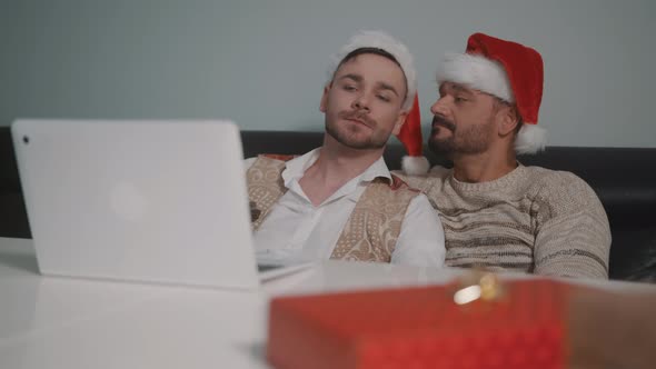 Young Caucasian Gay Couple with Santa Claus Hats Watching Movies on the Laptop on the Christmas Eve