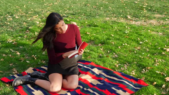 A beautiful hispanic woman college student reading a book and relaxing outdoors in the park with aut