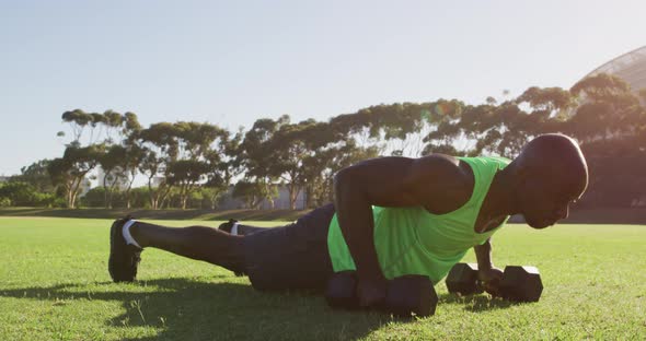 Fit african american man exercising outdoors doing press ups holding dumbbells