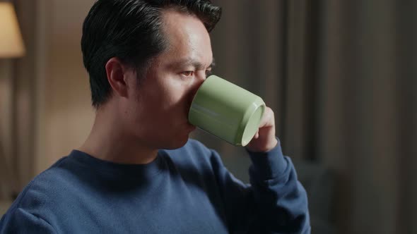 Side View Of Asian Male Engineer With The House Model Drinking Coffee While Working On A Desktop