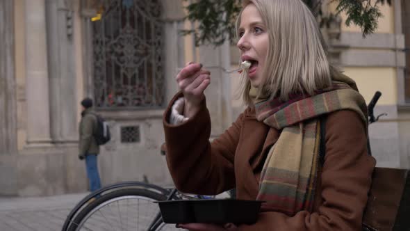 woman eating a salad on city bench