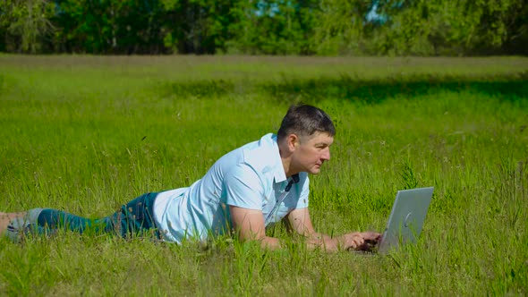 Businessman Works Behind a Laptop Lying on the Grass