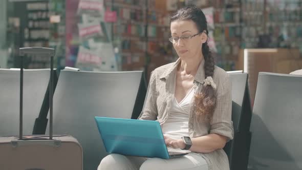 Mid-adult Caucasian Businesswoman Using Laptop, Checking Time on Watch and Leaving for Departure