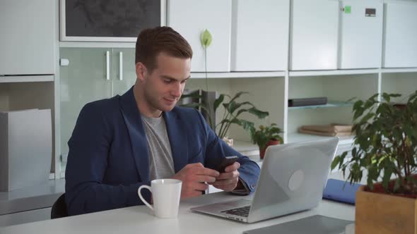 Young Businessman in the Modern Office Using App on Smartphone.