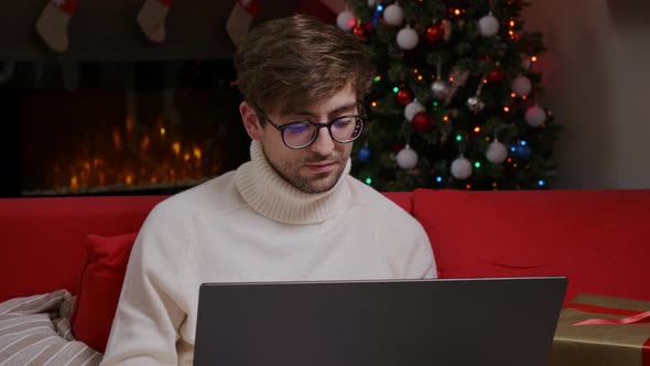 Young man freelancer in eyeglasses looking at laptop screen, working remotely at home.