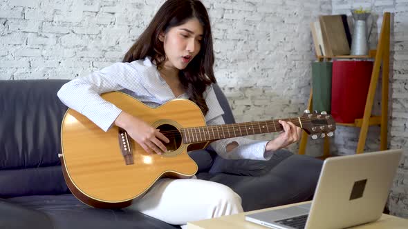Young Asian Woman Practicing How to Play Guitar on Laptop