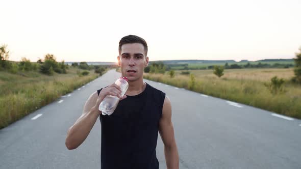 Young Sportsman Walking to Camera Looking Into It Drinking a Bottle of Water