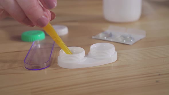 Hand with Tweezers Takes Out of the Container with the Solution of the Lens for the Eye