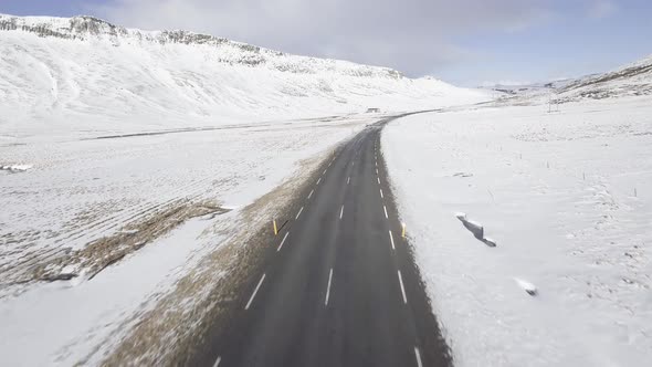 Aerial view of snowy landscape with icy road through the hills in Iceland