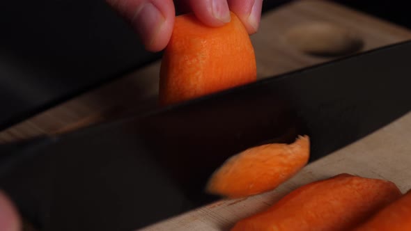 Chopping thin slices from a carrot with a black knife on a wooden cutting board.