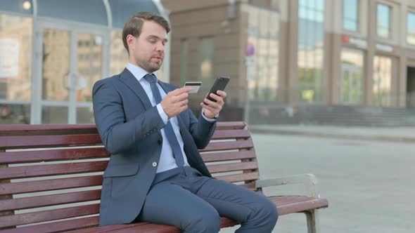 Excited Businessman Shopping Online via Smartphone, Sitting Outdoor