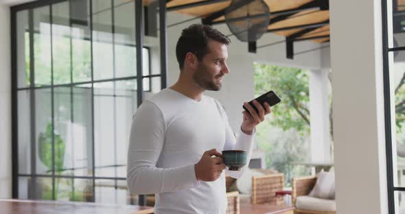 Man holding coffee cup and talking on mobile phone in a comfortable home 4k