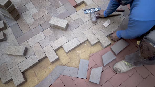 Putting brick pavers in place for the herringbone design in the two tone emblem, the artisan uses a