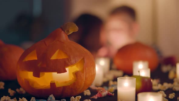 Carved Halloween Pumpkin Lantern on Table with Burning Candles and Sweets in Decorated Home