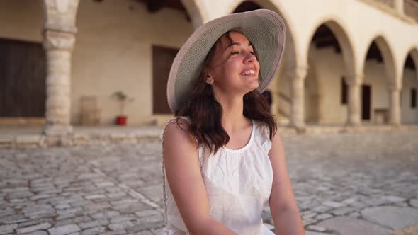 Medium Shot of Young Excited Woman in Straw Hat and White Dress Admiring Ancient Architecture