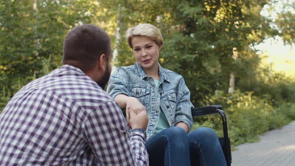 Woman is Sitting on Wheelchair and Talking to Man Holding Hands