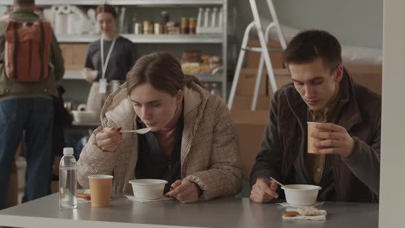 Young Couple of Refugees Eating Soup at Food Bank