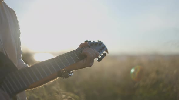 Man Guitarist Plays the Guitar in the Grassy Field at Sunset  Backlit Shot