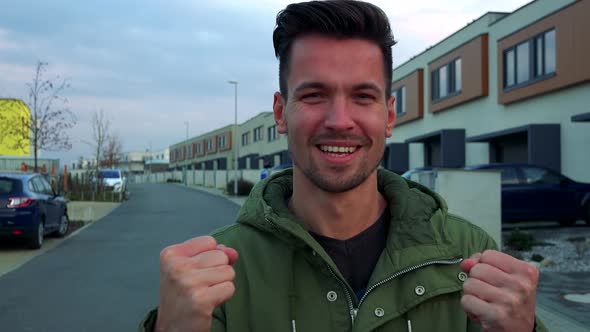 A Young, Handsome Man Stands on a Road in a Neighborhood and Celebrates, Fists Clenched