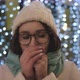 Beautiful brunette in glasses and a winter hat against the background of a garland. Waiting concept - VideoHive Item for Sale
