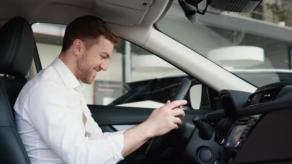 Portrait of a Happy Young Man Driving a New Luxury Electric Car in a Car Dealership