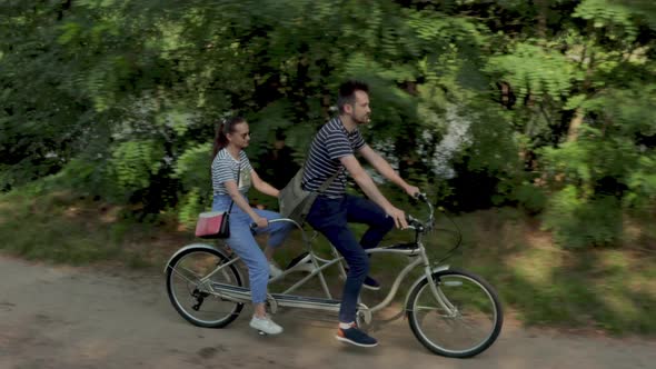 A young couple rides a tandem two-seater bike along the riverbank