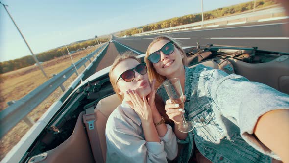 Two Beautiful Woman Drink Champagne, Relax and Have Fun in a Convertible, Using Smartphones, Taking