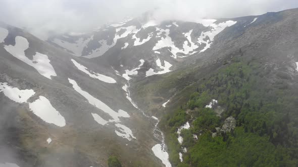 Aerial Forested Mountain With Snow Fragments Among The Clouds in The Spring