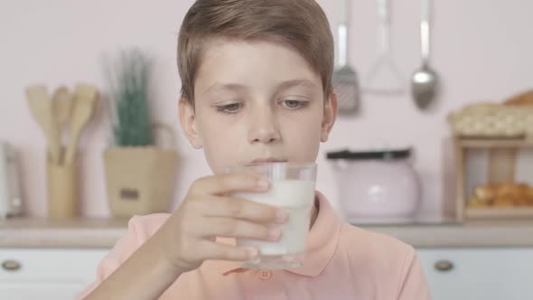 Close-up of Mischievous Little Boy Smelling Milk in Glass with Dissatisfied Facial Expression