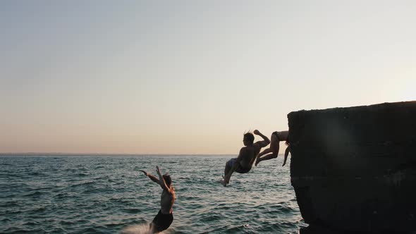 Group of Young Friends Jumping and Doing Tricks From a Pier Into the Sea During Beautiful Sunrise