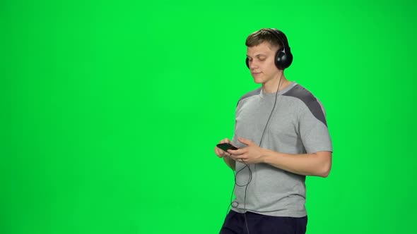 Man in Big Headphones Goes and Texting with Smartphone on Green Screen at Studio. Slow Motion