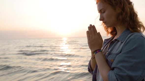 Young Lesbian LGBT Woman Prays During Sunset at Sea