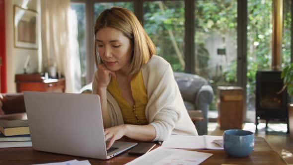 Asian woman sitting at table working from home and using laptop