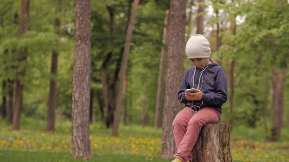 . A Cute Little Girl Enjoying Music with Smart Phone in the Park. Alone