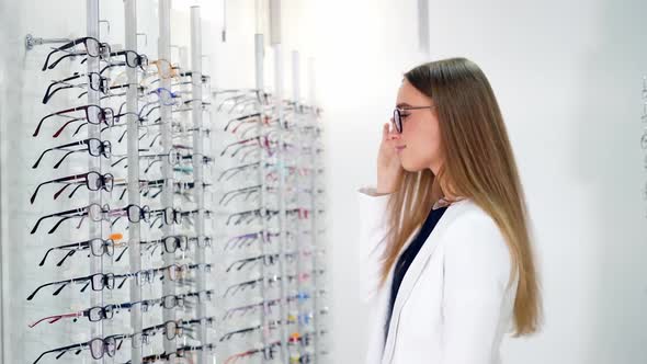 Woman in optical center trying eyeglasses. Cute girl deciding for glasses of different shapes and co