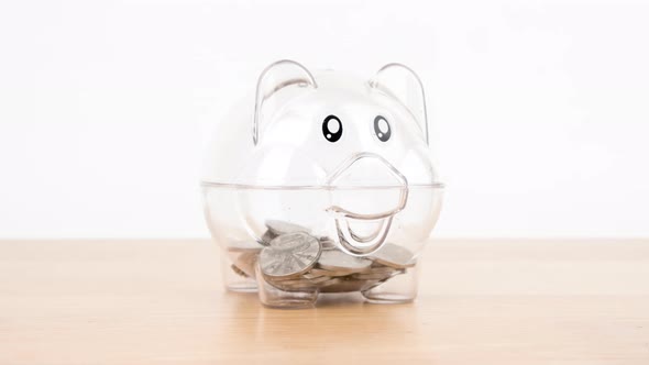 Stop motion animation coin into a piggy bank on wooden desk alt