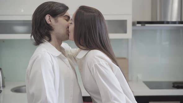 Loving Couple Kissing on Kitchen at Home. Side View Middle Shot of Handsome Man and Beautiful Woman