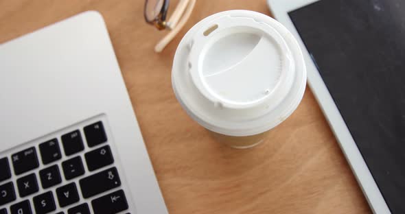 Close-up of spectacle, disposable coffee cup with laptop and digital tablet on desk