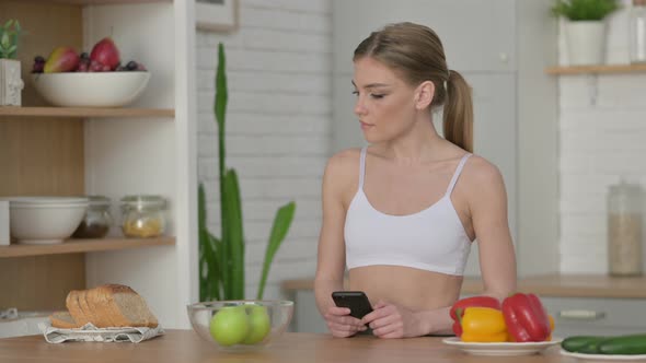 Athletic Woman Making Online Payment on Smartphone in Kitchen