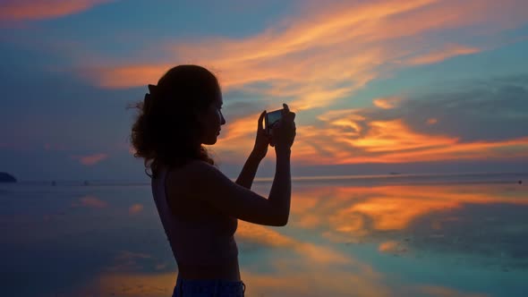 Tourist Woman Taking Photos with Mobile Phone Camera of Amazing Sunset at the Coats