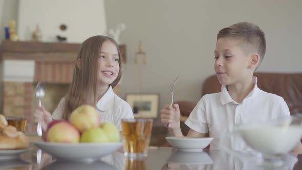 Twins Brother and Sister Are Sitting at the Table in a White Shirts Before School and Knocking with