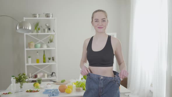 Happy Confident Caucasian Girl Showing Weight Loss in Too Big Jeans