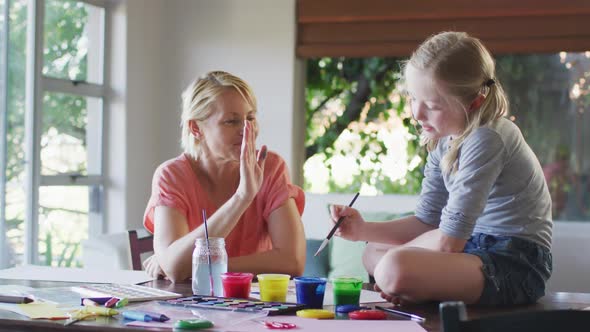 Side view of Caucasian woman painting with her daughter at home and giving a high five