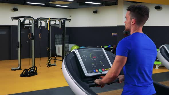 A Young Fit Man Walks on a Treadmill in a Gym - Closeup From Behind